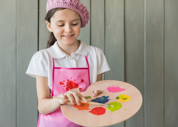 Kostenloses Foto porträt eines mädchens, welches die farbe auf palette mit pinsel mischt