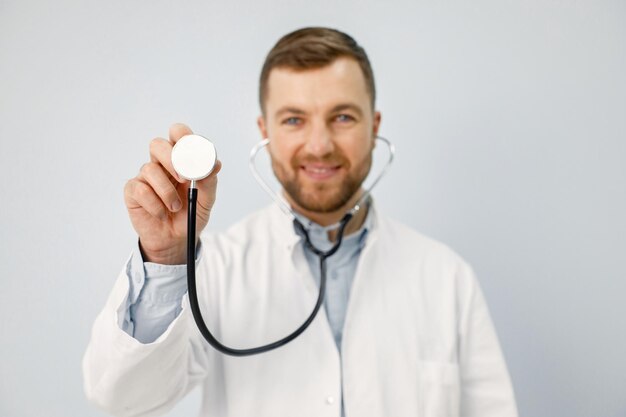 Porträt eines männlichen Arztes, der in die Kamera schaut, die ein Stethoskop hält