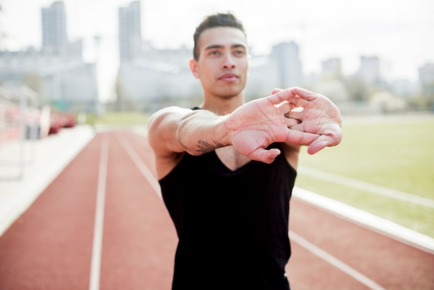 Porträt eines männlichen Athleten, der ihre Hände bevor dem Laufen auf Rennstrecke ausdehnt
