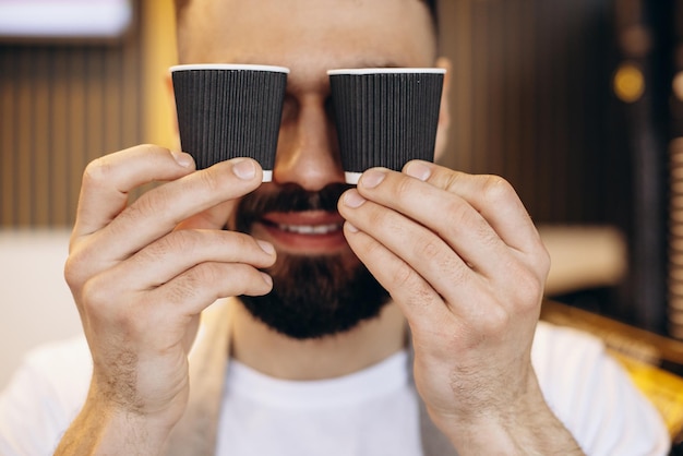 Kostenloses Foto porträt eines männlichen barista, der espressotassen aus pappe hält und lächelt