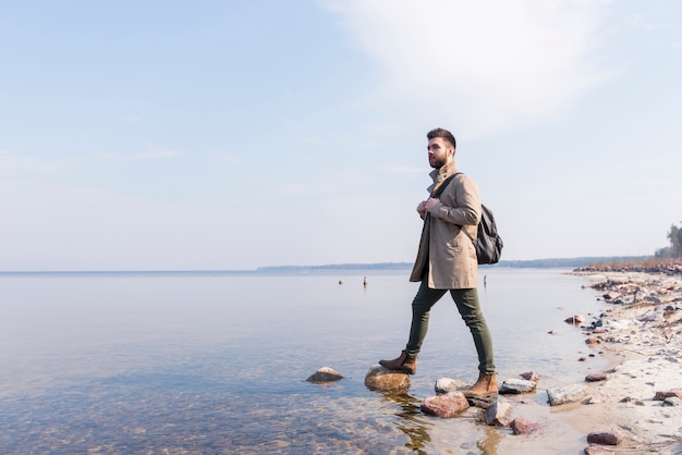 Porträt eines männlichen Reisenden, der nahe dem See mit seinem Rucksack steht