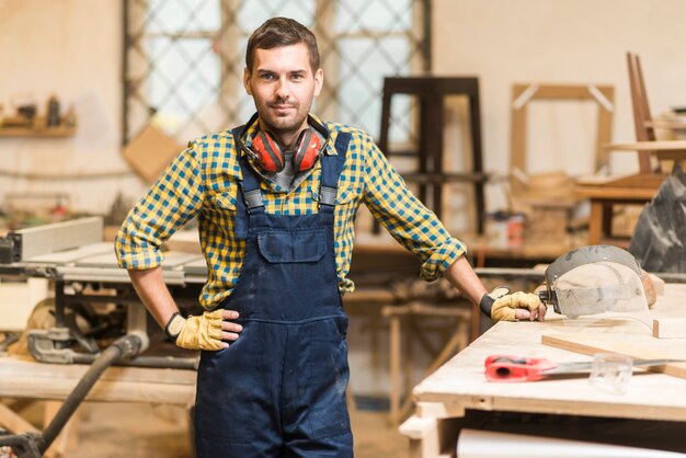 Porträt eines männlichen Tischlers mit seiner Hand auf der Hüfte, die nahe dem Werktisch steht