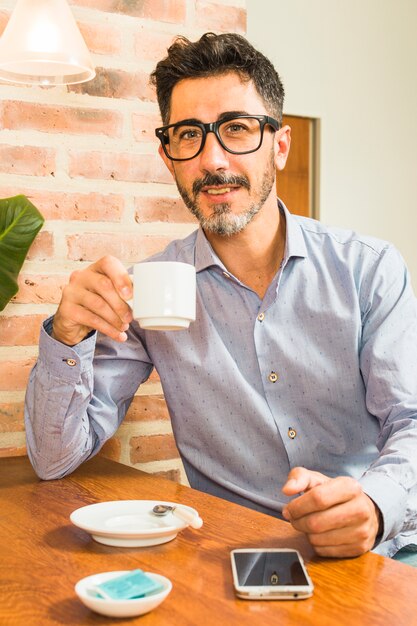 Porträt eines Mannes, der in der Hand Kaffeetasse mit Handy auf Tabelle hält