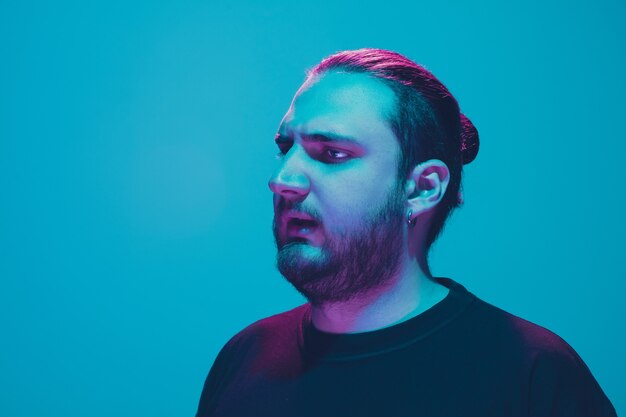 Porträt eines Mannes mit buntem Neonlicht an blauer Wand. Männliches Model mit ruhiger und ernster Stimmung. Gesichtsausdruck, Millennials Lifestyle und Aussehen. Zukunft, Technologien.