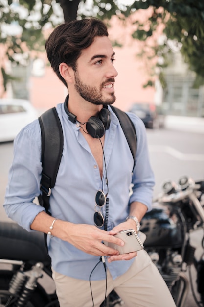 Kostenloses Foto porträt eines mannes mit dem smartphone, der vor motorrad steht