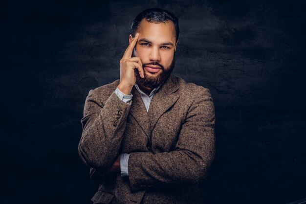 Porträt eines nachdenklichen afroamerikanischen Mannes, gekleidet in eine klassische braune Jacke, die in einem Studio auf dunklem Hintergrund steht.