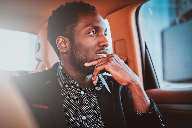 Porträt eines nachdenklichen, eleganten Afro-Etnicity-Geschäftsmanns im Auto als Beifahrer.
