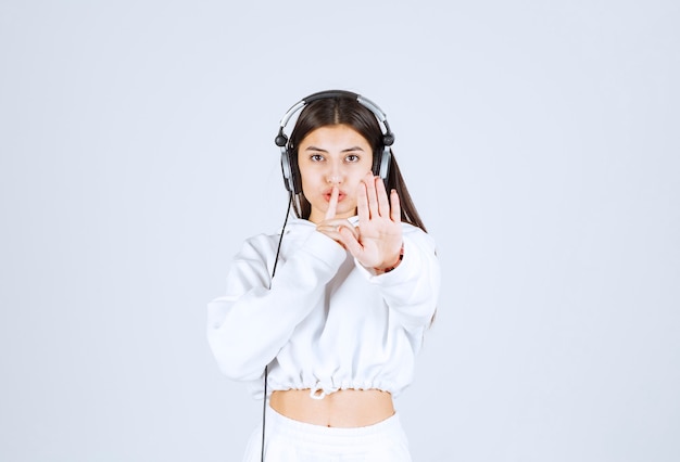 Porträt eines netten Modells des jungen Mädchens mit Kopfhörern, die stilles Zeichen zeigen.