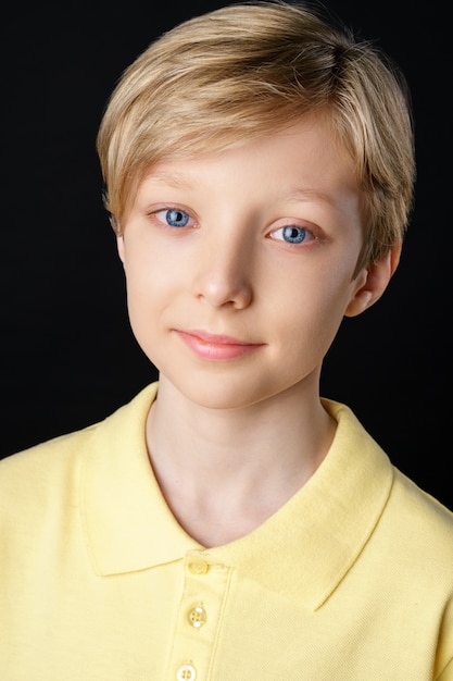 Porträt eines niedlichen Jungen in einem gelben T-Shirt auf einem schwarzen Hintergrund, der für die Kamera aufwirft