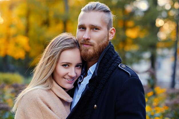 Porträt eines Paares auf einem Datumsspaziergang im Herbstpark hautnah. Positiver rothaariger bärtiger Mann umarmt die süße blonde Frau.