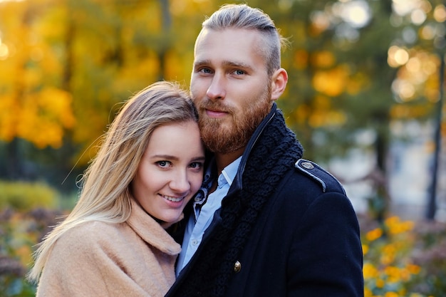 Porträt eines Paares auf einem Datumsspaziergang im Herbstpark hautnah. Positiver rothaariger bärtiger Mann umarmt die süße blonde Frau.