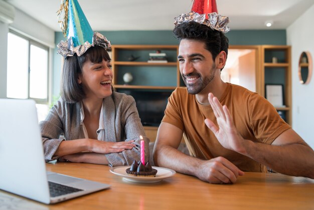 Porträt eines Paares, das Geburtstag auf einem Videoanruf mit einem Laptop von zu Hause feiert. Paar feiert Geburtstag online in Quarantänezeit. Neues normales Lifestyle-Konzept.