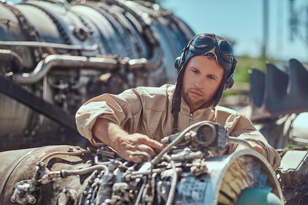 Porträt eines Piloten-Mechanikers in Uniform und fliegendem Helm, der in einem Freilichtmuseum die zerlegte Flugzeugturbine repariert.