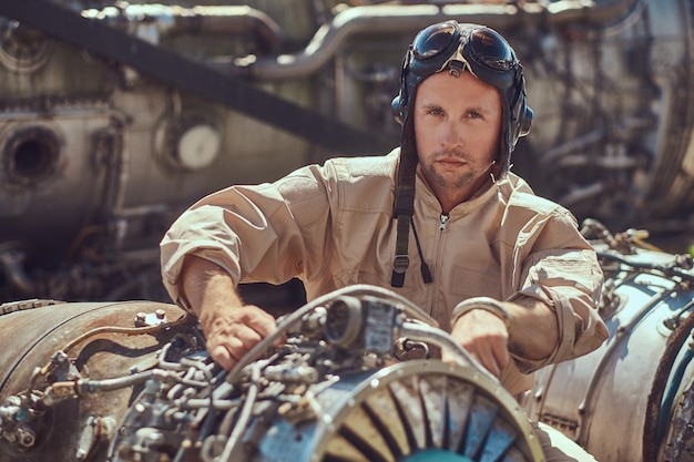 Porträt eines Piloten-Mechanikers in Uniform und fliegendem Helm, der in einem Freilichtmuseum die zerlegte Flugzeugturbine repariert.