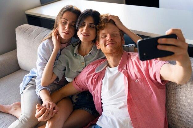 Porträt eines polyamourösen Paares zu Hause, das ein Selfie auf der Couch macht