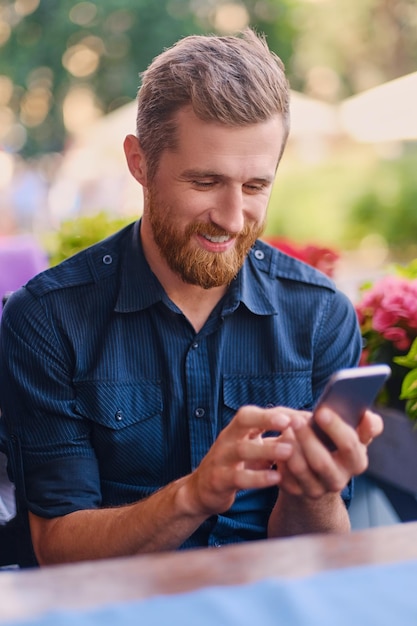 Porträt eines positiven rothaarigen bärtigen Mannes, der ein Smartphone verwendet.