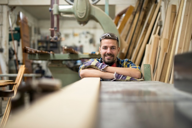 Kostenloses Foto porträt eines professionellen holzarbeiters, der neben einer maschine und holzmaterial in seiner tischlerei steht