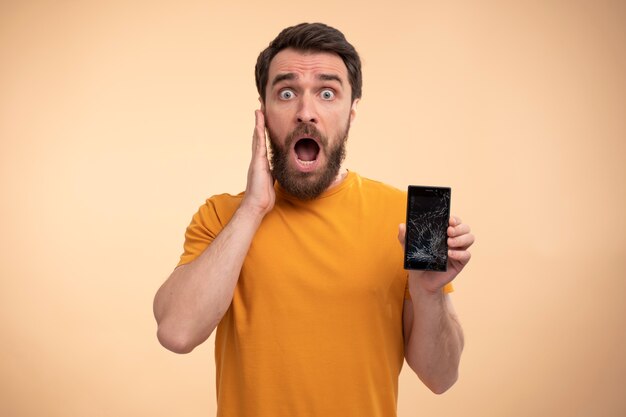 Porträt eines schockierten jungen Mannes, der sein Smartphone zeigt