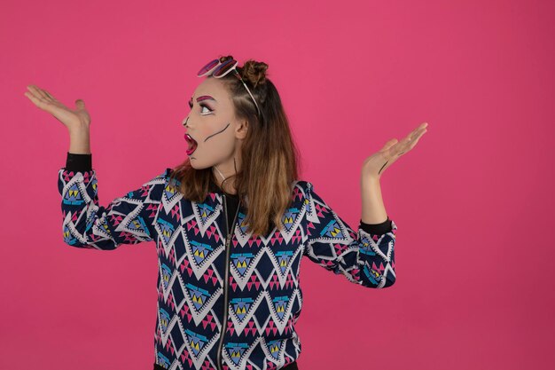 Porträt eines schockierten Mädchens, das kreatives Make-up trägt und ihre Hände hochhält. Foto in hoher Qualität