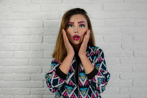 Porträt eines schockierten Mädchens, das kreatives Make-up trägt und sich die Hände vors Gesicht hält. Foto in hoher Qualität