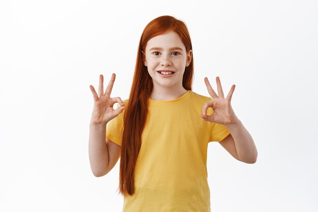 Porträt eines schönen Kindes, Mädchen mit rotem Kopf und Sommersprossen zeigt okayzeichen und lächelt glücklich