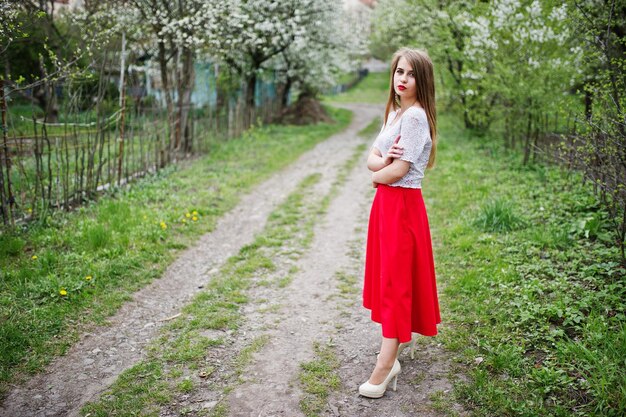 Porträt eines schönen Mädchens mit roten Lippen im Frühlingsblütengarten auf rotem Kleid und weißer Bluse