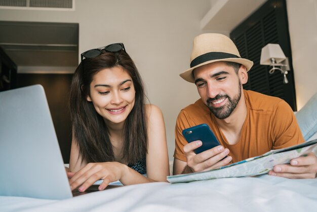 Porträt eines schönen Paares, das seine Reise mit Laptop und Handy im Hotelzimmer organisiert?