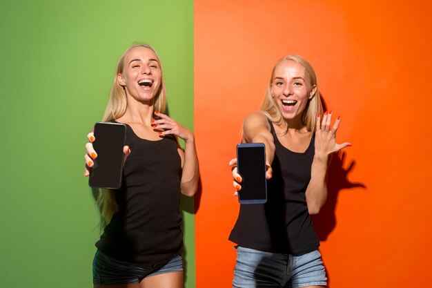 Porträt eines selbstbewussten lässigen Mädchens, das Handy des leeren Bildschirms lokalisiert über buntem Hintergrund zeigt