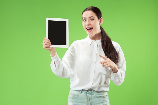 Porträt eines selbstbewussten lässigen Mädchens, das leeren Bildschirm des Laptops lokalisiert über grünem Hintergrund zeigt.