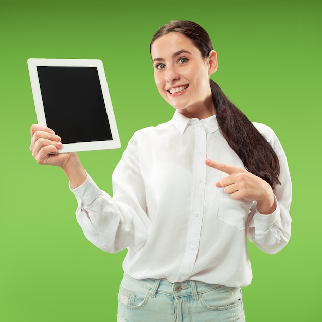 Porträt eines selbstbewussten lässigen Mädchens, das leeren Bildschirm des Laptops lokalisiert über grünem Hintergrund zeigt.
