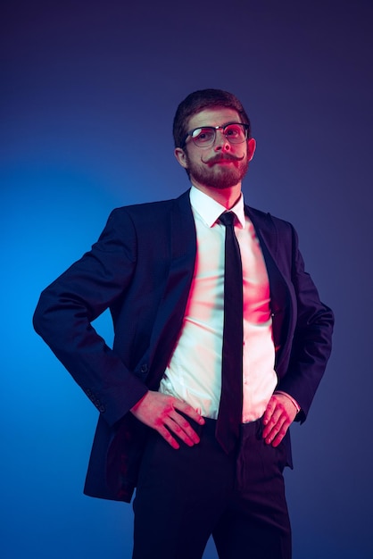 Porträt eines stilvollen Mannes mit Schnurrbart im offiziellen Anzug, der isoliert vor blauem Studiohintergrund im Neonlicht posiert