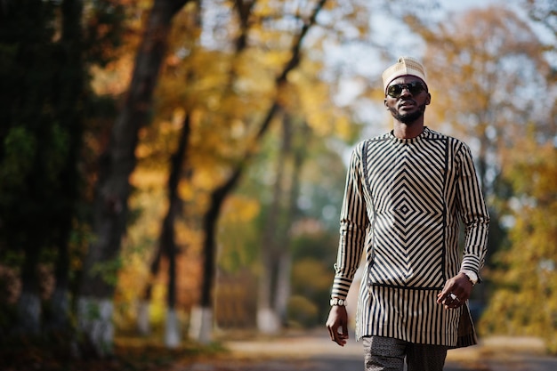 Porträt eines stilvollen schwarzen afroamerikanischen Mannes mit Hut und Sonnenbrille vor sonnigem Herbsthintergrund Reiche Menschen in Afrika in traditioneller Kleidung