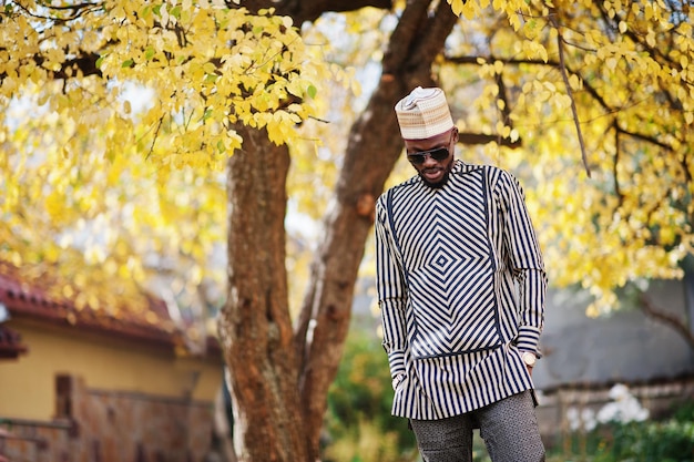 Porträt eines stilvollen schwarzen afroamerikanischen Mannes mit Hut und Sonnenbrille vor sonnigem Herbsthintergrund Reiche Menschen in Afrika in traditioneller Kleidung