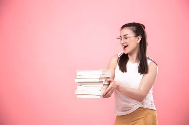 Porträt eines Studentenmädchens mit Brille auf einem rosa Hintergrund, der mit Büchern in ihren Händen aufwirft. Bildungskonzept und Hobbys.