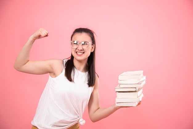Porträt eines Studentenmädchens mit Brille auf einem rosa Hintergrund, der mit Büchern in ihren Händen aufwirft. Bildungskonzept und Hobbys.