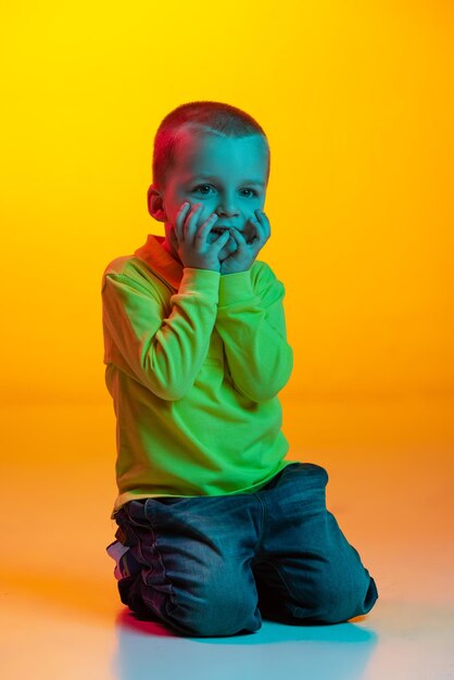 Porträt eines süß aussehenden kleinen Jungen, der isoliert vor gelbem Hintergrund in Neonlicht posiert