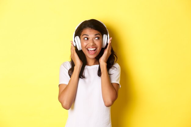 Porträt eines süßen afroamerikanischen Mädchens, das lächelt, während es Musik in Kopfhörern hört und beiseite schaut