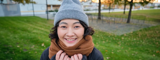 Kostenloses Foto porträt eines süßen asiatischen mädchens mit mütze und schal, das bei kühlem frühlingswetter lächelnd und lächelnd durch die stadt spaziert