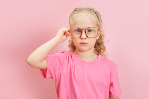 Porträt eines süßen kaukasischen vorschulmädchens in einem rosa t-shirt, das die brille auf der nase glättet, augenheilkundekonzept für kinder, zurück zur schule