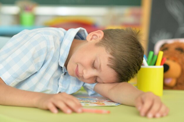 Porträt eines süßen kleinen jungen, der im klassenzimmer auf dem tisch schläft
