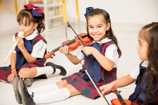 Kostenloses Foto porträt eines süßen lateinamerikanischen mädchens, das lernt, wie man geige spielt und spaß in der vorschule hat