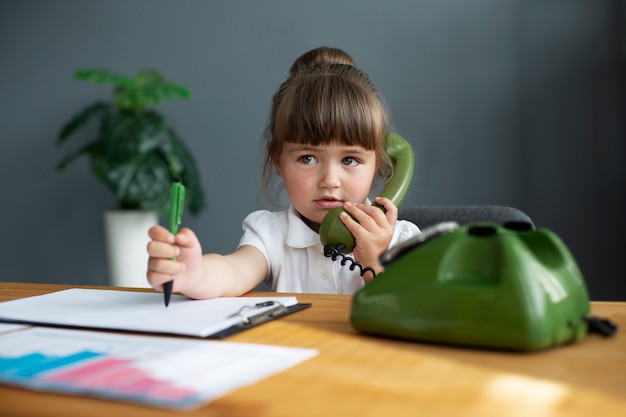 Porträt eines süßen Mädchens, das an ihrem Schreibtisch ein Telefon mit Wählscheibe verwendet
