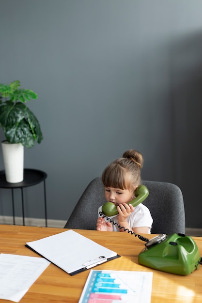 Kostenloses Foto porträt eines süßen mädchens, das im büro am telefon mit wählscheibe spricht