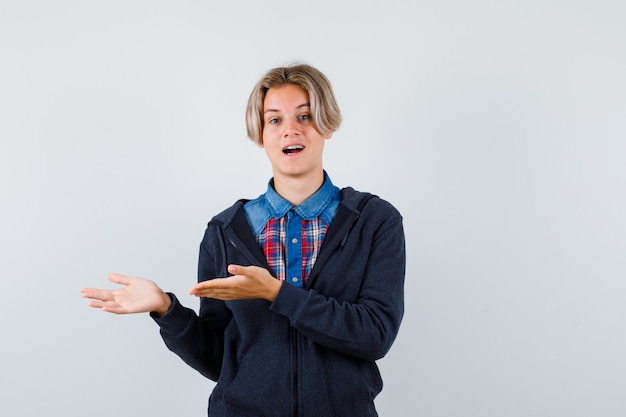 Porträt eines süßen Teenagers, der eine einladende Geste in Hemd, Hoodie zeigt und sich wunderte Vorderansicht