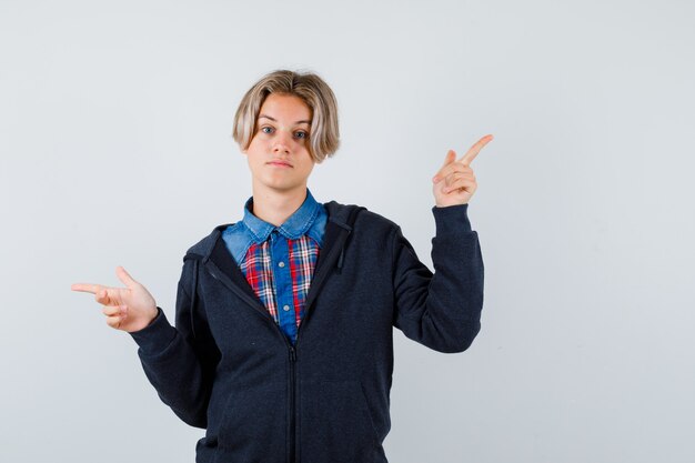 Porträt eines süßen Teenagers, der nach rechts und links in Hemd, Hoodie zeigt und nachdenkliche Vorderansicht schaut