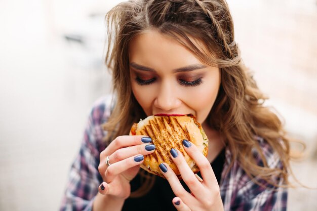 Porträt eines Teenager-Mädchens mit welligem Haar, das mit Schock oder Überraschung zur Seite schaut und bereit ist, einen Burger in ihre Hände zu beißen.
