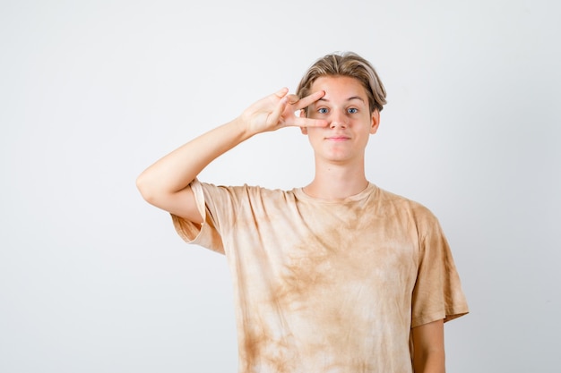 Porträt eines teenagers, der ein v-zeichen auf dem auge im t-shirt zeigt und eine fröhliche vorderansicht sieht