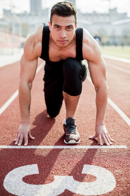 Porträt eines überzeugten männlichen Athleten auf der Startlinie der Rennstrecke