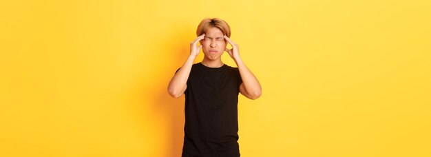 Porträt eines unruhigen asiatischen männlichen studenten, der kopfschmerzen hat, die vor schmerzen grimassen schneiden und den kopf berühren