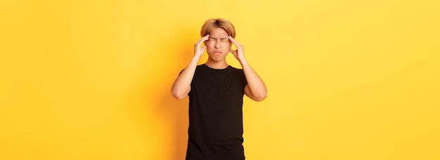 Porträt eines unruhigen asiatischen männlichen Studenten, der Kopfschmerzen hat, die vor Schmerzen Grimassen schneiden und den Kopf berühren